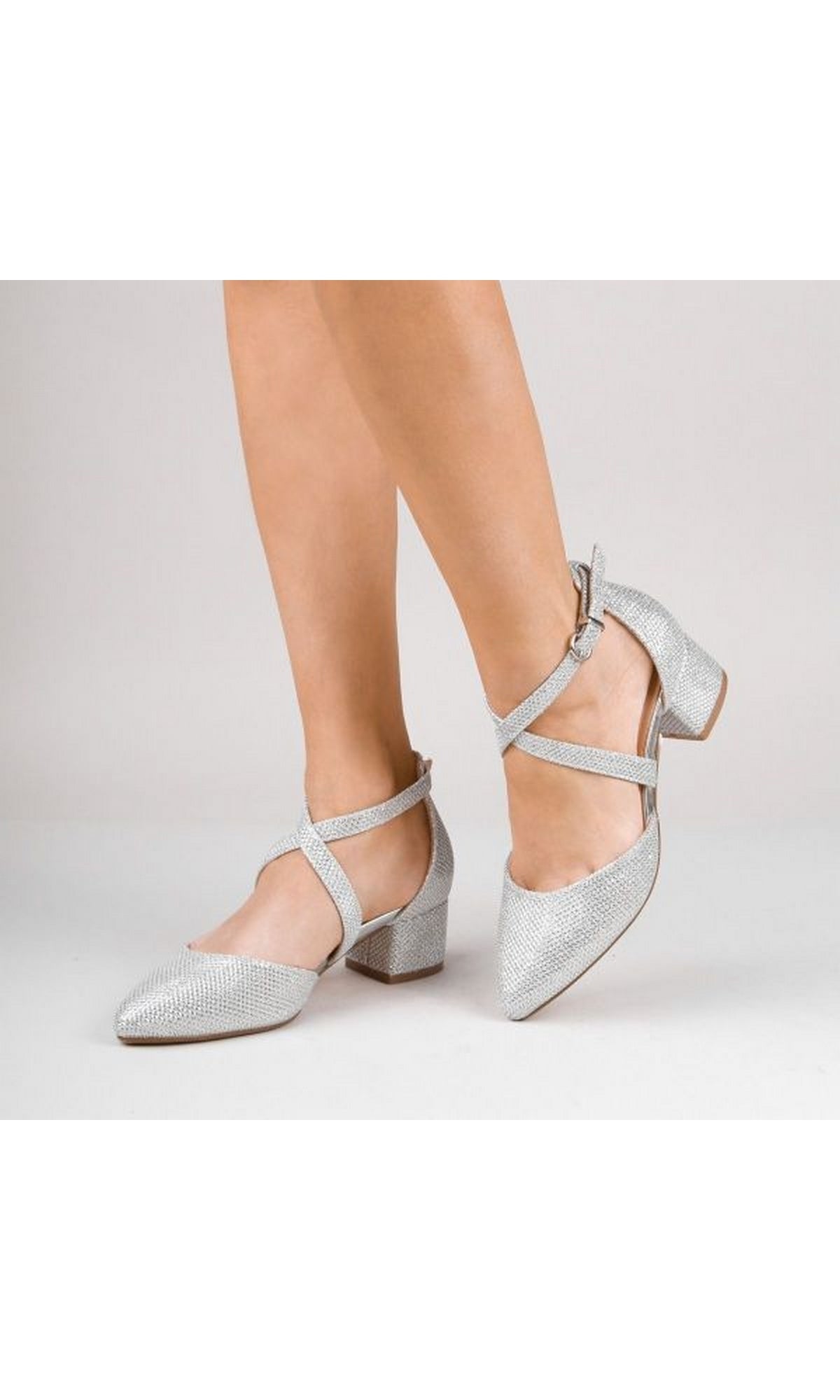 A person wearing Francis Silver P2228 Silver Closed-Toe Prom Shoes with low heels, pointed toes, and ankle straps against a plain background.